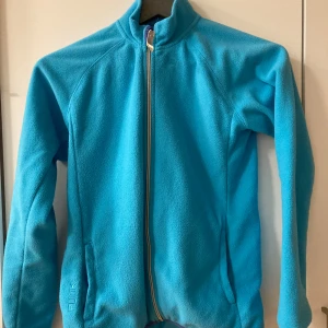 Blå fleecejacka från 157 Funk - Blå fleecejacka från 157 Funk med hel dragkedja framtill och två fickor. Jackan har hög krage och är långärmad, perfekt för kyliga dagar. Mjuk och skön känsla tack vare fleecematerialet. Snygg och enkel design. Från djurfritt rökfritt och parfymfritt hem. 