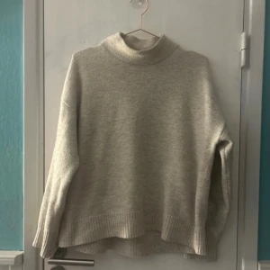 Beige polotröja i stickad ull - Mysig beige polotröja i stickad ull med lång ärm och ribbade muddar. Tröjan har en avslappnad passform och hög krage som håller dig varm under kyliga dagar. Perfekt att slänga på sig när det är lite kallare ute. Lite nopprig annars fint skick