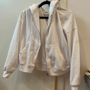 Vit hoodie från FB Sister med dragkedja - Vit hoodie från FB Sister i storlek XXS. Tröjan har huva med snörning, två stora fickor framtill och hel dragkedja. 