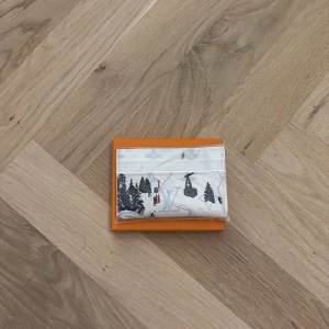 Vit plånbok med snömotiv - Snygg vit plånbok med vinterinspirerat motiv av skidåkare, träd och liftar. Plånboken har flera fack för kort och är tillverkad i exklusivt skinn med tryckt design. Perfekt för dig som gillar unika accessoarer med coola detaljer.