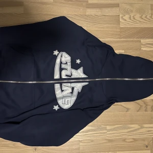 Mörkblå hoodie från 4tune med tryck - Säljer en mörkblå hoodie från 4tune med coolt tryck i silver på både fram- och baksidan. Hoodien har huva, lång ärm och en stor dragkedja framtill. Materialet känns mjukt och skönt, perfekt för chill dagar. Trycket har stjärnor och logga i futuristisk stil.