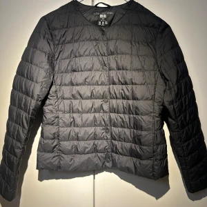Svart dunjacka från Uniqlo XXS - Säljer en svart, lätt dunjacka från Uniqlo i storlek XXS. Jackan har rund hals, raka linjer och knäppning med svarta knappar framtill. Perfekt för dig som vill ha en clean och enkel look under höst och vinter. Jag är öppen för prisförslag!🩷