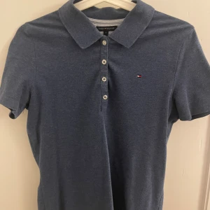 Blå klassisk pikéskjorta Tommy Hilfiger - Snygg blå pikéskjorta från Tommy Hilfiger i klassisk passform. Skjortan har korta ärmar, krage och fyra knappar framtill. Liten broderad logga på bröstet ger en stilren touch. Perfekt för dig som gillar enkel och tidlös design.