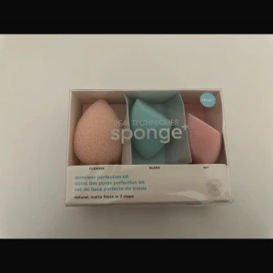 Real Techniques Sponge+ Poreless Kit - Säljer ett Real Techniques Sponge+ poreless perfection kit med tre olika makeupsvampar. En persikofärgad rengöringssvamp, en ljusblå blending-svamp och en rosa setting-svamp. .