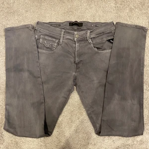 Replay Anbass Jeans  - Säljer ett par gråa Replay jeans i slim fit-modell. Byxorna har klassisk femficksdesign, dragkedjegylf och Replay-logga på fickan. Snygg, smal passform och tillverkade i mjukt bomullsmaterial med lite stretch för extra komfort.