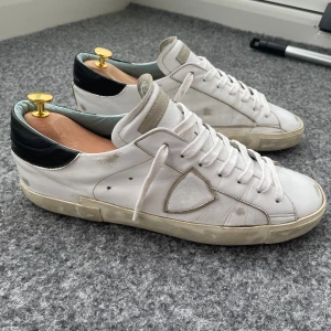 Philippe Model stl 44 - Snygga vita sneakers från Philippe Model Paris med svart hälparti och grå detaljer. Skorna har rund tå, platt sula och klassisk snörning. Tillverkade i skinn med logotyp på sidan och bak. Perfekt för dig som gillar stilrena och exklusiva sneakers. De har släppt på sidorna men det har jag lagat. Sulorna är inte så slitna. Hör av dig vid frågor😊