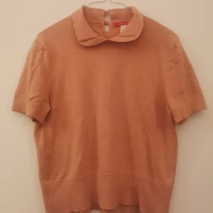 Rosa finstickad kortärmad tröja - Supersöt rosa tröja från Anne Klein med korta ärmar och en rund, mjuk krage. Tröjan har knäppning bak i nacken och är tillverkad i en lyxig mix av silke, nylon och kashmir. Perfekt för dig som gillar en clean och klassisk look med en twist.