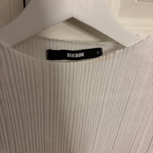 Vit ribbad långärmad tröja Bikbok - Säljer en vit långärmad tröja från Bikbok i storlek S. Tröjan har ett ribbat tyg med smala vertikala ränder och en enkel, rund halsringning. Materialet är mjukt och stretchigt, vilket gör den skön att bära. Perfekt att styla med jeans eller kjol.