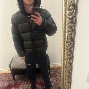 Svart pufferjacka från Zara med huva - Säljer en svart pufferjacka från Zara i storlek M. Jackan har en schysst oversized look, huva och dragkedja framtill. Materialet är glansigt syntet och jackan är riktigt fluffig och varm, perfekt för kalla dagar. Enkelt att matcha med streetwear.