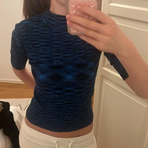 Blåmönstrad tight topp med halvärm - Säljer en tight topp i blått och svart med coolt abstrakt mönster. Toppen har halvärm och hög hals, sitter figurnära och är perfekt för dig som gillar en modern och sportig look. Materialet känns stretchigt och bekvämt.