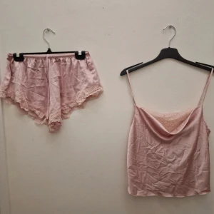 Ljusrosa pyjamas  - Säljer en ljusrosa topp med tunna axelband och snygg draperad halsringning, och tillhörande shorts. Materialet är mjukt och glansigt, perfekt för chill hemma eller mysiga kvällar. Endast provad & tvättad