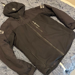 Svart vinterjacka från Sail Racing - Svart vinterjacka från Sail Racing. Materialet är slitstarkt, vattenavvisande, och klarar av starka vindar. Den är dunfodrad och klarar av kalla vinterdagar. Perfekt för dig som vill klara av all väder i en och samma jacka. Jag är 187cm för referens, den är i utmärkt skick, köpt på stadium för 4000kr, mitt pris 1600