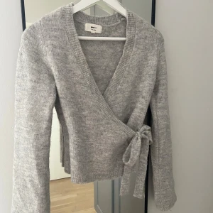 Grå omlottkofta från Gina Tricot - Supermysig grå stickad omlottkofta från Gina Tricot med knyt i sidan & v-ringad hals. Koftan har lång ärm & ribbade kanter, perfekt för höst & vinter 💗