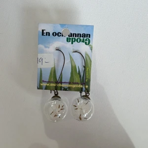 Örhängen med maskrosfrön i glaskula - Unika örhängen från En och annan groda med maskrosfrön inneslutna i klara glaskulor. Hängande modell med metallkrok i antikbronsfärg. Perfekt för dig som gillar naturinspirerade smycken och vill ha något annorlunda.