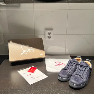 Christian Louboutin mörkblå mockasneakers - Exklusiva sneakers från Christian Louboutin i mörkblå mocka med klassisk röd sula. Skorna har rund tå, platt sula och snörning. Kommer med originalkartong, dustbag och äkthetsbevis. Perfekta för dig som vill sticka ut med lyxig streetstyle.