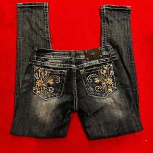 Miss Me skinny jeans med broderi - Snygga mörkblå skinny jeans från Miss Me med coolt guldigt broderi på bakfickorna och slitningar framtill. Jeansen har vita kontrastsömmar, klassisk femficksdesign och metallknappar. Perfekt skick inget slitage. Storlek 28