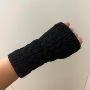 Svarta stickade tumlösa vantar - Svarta stickade tumlösa vantar med flätmönster. De är ribbade vid kanterna och har en klassisk, enkel design som passar perfekt när du vill hålla händerna varma men ändå kunna använda mobilen. Snygga och praktiska för kyliga dagar.
