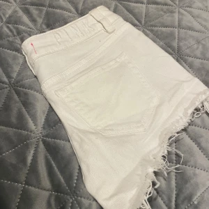 Vita jeansshorts från PINK - Snygga vita jeansshorts från PINK med råa, fransiga kanter och klassisk femficksdesign. Shortsen har broderad logga på linningen och silverfärgad knapp med PINK-tryck. Perfekta för sommarens alla äventyr!