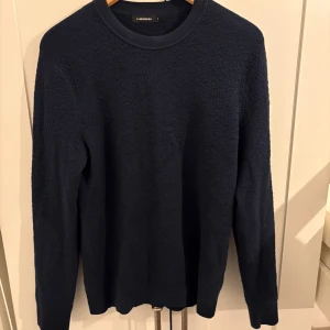 Mörkblå stickad tröja J.Lindeberg - Säljer en mörkblå stickad tröja från J.Lindeberg i storlek M. Tröjan har rund halsringning och lång ärm, perfekt för kyligare dagar. Enkel och stilren design som funkar till det mesta. Materialet är mjukt och ger en skön känsla.