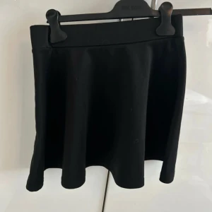 Svart kortkjol barn  - Säljer en svart kortkjol från Kappahl med enkel och stilren design. Kjolen har en lätt utsvängd form och bred linning som sitter bekvämt i midjan. Perfekt att matcha med sneakers eller boots för en cool look.