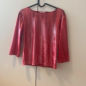 Röd glittrig topp från Hennes Collection - Säljer en röd glittrig topp från Hennes Collection. Toppen har trekvartsärm och en rak, enkel passform. Materialet är glansigt och skimrande, perfekt för att sticka ut. Snygg att styla med både jeans och kjol.