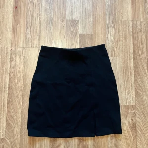 Svart kortkjol från Gina Tricot XS - Svart, stilren kortkjol från Gina Tricot i storlek XS. Kjolen har en rak passform och en liten slits framtill 