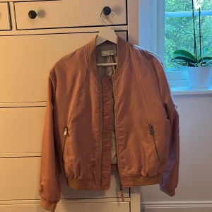 Rosa bomberjacka från Zara Basic - Snygg rosa bomberjacka från Zara Basic i storlek S. Jackan har ribbade muddar, två fickor med dragkedja och klassisk bomberkrage. Materialet är syntet och jackan har en stilren look som passar perfekt till streetwear. Färgen är ljusrosa och modellen är loose fit.