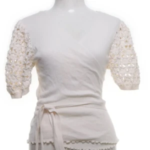 Vit omlottopp med spetsärmar - Säljer en vit omlottopp med korta ärmar i spets och knytband i midjan. Toppen har en feminin v-ringning och dekorativa kanter längst ner. Perfekt för dig som gillar romantiska detaljer och en ljus, fräsch look.