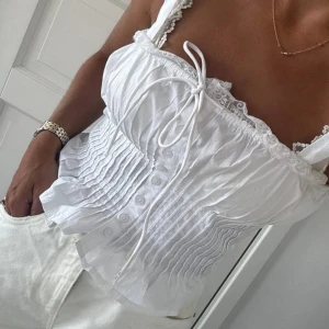 Vit korsett-topp med spets och knyt - Säljer min supersöta vita korsett-topp med knytbara axelband, spetsdetaljer och knappar framtill eftersom att den inte längre kommer till användning. Mycket bra skick då den endast har använts en gång. Köpte den för 399kr. 