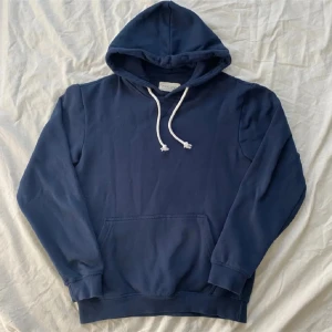 Mörkblå hoodie från Pier One - Mörkblå hoodie från Pier One med klassisk känguruficka och vita snören i huvan. Tröjan har lång ärm och ribbade muddar. Perfekt för dig som gillar en enkel och stilren look. Materialet är mjukt och skönt, troligtvis bomull eller bomullsblandning.