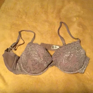 Lila spets-bh från Lelle May - Säljer en snygg lila bh från Lelle May med vacker spets över hela kuporna. Bh:n har justerbara axelband och klassisk knäppning bak. Perfekt för dig som gillar romantiska detaljer och en feminin look.