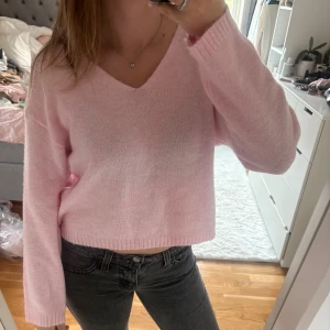 Ljusrosa stickad tröja med v-ringning - Superfin ljusrosa stickad tröja med v-ringad hals och lång ärm. Modellen är lite croppad och har ribbade muddar vid ärmslut och nederkant. Perfekt att matcha med jeans för en chill look. Mjuk och skön, passar dig som gillar pastellfärger.