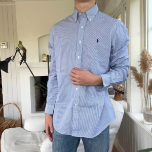 Blårandig skjorta från Ralph Lauren - Klassisk blårandig skjorta från Ralph Lauren i bomull. Skjortan har button-down krage, broderad logga på bröstet och lång ärm. Classic fit med vita knappar och stilren look, perfekt till jeans eller chinos.