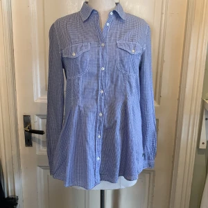 Blårutig långärmad skjorta - Snygg blårutig skjorta med klassisk krage och knappar framtill. Skjortan har två bröstfickor med lock och vita knappar. Den är långärmad och har en insvängd passform som sitter skönt. Perfekt för dig som gillar en chill och stilren look.