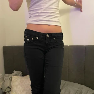 Svarta True Religion jeans bootcut/raka - Svarta jeans från True Religion med låg midja och bootcut/raka. Snygga silverfärgade knappar och detaljer på fickorna, klassisk True Religion patch bak. Jeansen har raka ben med lätt utsvängning och är gjorda i jeansmaterial.