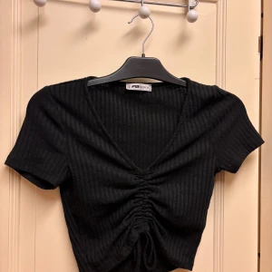 Svart croppad topp från New Yorker S - Svart croppad topp från New Yorker i storlek S. Toppen har korta ärmar och snygg snörning framtill som ger en rynkad effekt. Väldigt fin o skön! Knappast använd.