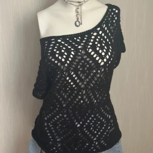 Svart virkad topp från Bondelid - Svart virkad topp från Bondelid med korta ärmar och snyggt mönster i geometriska former. Toppen har en loose passform och är lätt transparent med en cool offshoulder-look. Perfekt att styla med jeans eller shorts för en chill vibe.