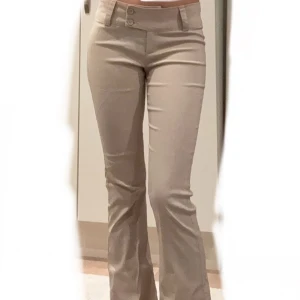 Beiga bootcut kostymbyxor - Snygga beiga kostymbyxor med bootcut-snitt och mid-waist från gina. Byxorna har två knappar framtill och bälteshällor. De är figurnära upptill och utsvängda nertill, vilket ger en modern och stilren look. OBS!! Har sprättat upp de. Byxorna är alltså ca 4 cm längre än vanligtvis! Knappt använda!! 