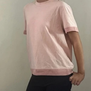 Ljusrosa t-shirt med meshdetaljer - Säljer en ljusrosa t-shirt i bomull med korta ärmar och snygga meshdetaljer vid ärmslut och nederkant. T-shirten har en loose passform och är perfekt för en chill och avslappnad stil.