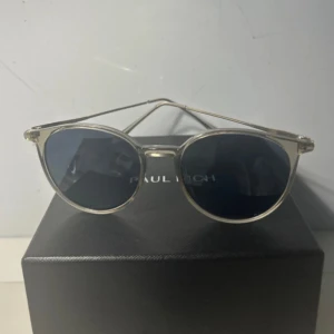  runda solglasögon silver - Snygga runda solglasögon från Paul Rich med tunna, silvriga bågar och mörka linser. Klassisk och stilren design som passar perfekt till sommaren. Lätta att matcha med olika outfits och ger en cool vibe.