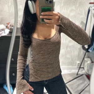 Brun ribbad långärmad topp - Säljer en brun långärmad topp med fyrkantig ringning och ribbad struktur. Ärmarna har en slitsdetalj vid handleden, materialet är mjukt och stretchigt.