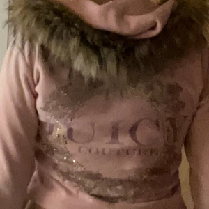 Rosa Juicy Couture teddyjacka  - Mysig rosa teddyjacka från Juicy Couture med glittrig logga på ryggen och huva med fuskpäls. Jackan har dragkedja framtill och två fickor. I nästan ny skick