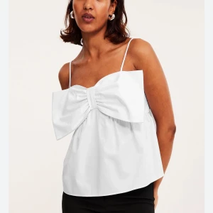 Vit linnetopp med stor rosett - Supersöt vit linnetopp med tunna axelband och en stor rosett framtill som verkligen sticker ut. 🩷