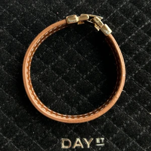 Brunt armband från DAY ET med guldspänne - Snyggt armband i brunt från h&m med dubbla remmar i skinnimitation och dekorativa vita sömmar. Stängs med ett coolt guldigt spänne som ger en lyxig känsla. Perfekt accessoar för att lyfta din outfit.