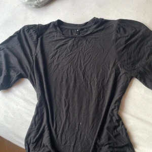 Svart t-shirt med längre ärmar från 157 - Svart t-shirt från 157 i mjuk bomull med korta puffärmar och rund hals. Enkel och stilren modell som passar till det mesta. Perfekt basplagg för dig som gillar en clean look.