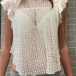 Vit spetsblus från Nelly - Säljer en vit blus från Nelly i storlek S. Blusen är genombruten med spets och har ett randigt mönster. Den har korta volangärmar och en croppad passform..