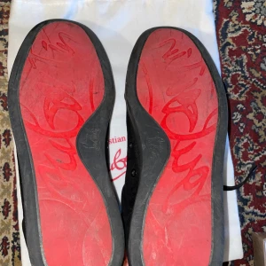 Christian Louboutin svarta sneakers mocka - Snygga svarta sneakers från Christian Louboutin i mjuk mocka med klassisk röd sula och svarta snören. Skorna har rund tå och platt sula, perfekt för dig som vill sticka ut med exklusiv design och streetkänsla. Kommer med originalpåse och box. Vådligt använda så du köper de medvetandes samt, har vi ett hål som syns på bilden men de inga större problem med den är använda där av priset 