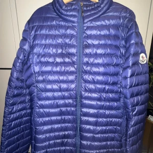 Blå dunjacka från Moncler - Säljer en blå dunjacka från Moncler med klassisk quiltad design och hög krage. Jackan har dragkedja framtill och Moncler-logga på ärmen. Säljer jackan då den blivit för liten kom priv för fler detaljer, pris går att sänka vid snabb affär 💕💕