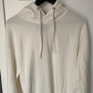 Vit hoodie från 157 i bomull - Säljer en stilren vit hoodie från 157 i storlek M. Tröjan har huva med snörning och är tillverkad i mjuk bomull. Perfekt för en chill look och passar året runt. Klassisk passform och ribbade muddar vid ärmslut och nederkant.