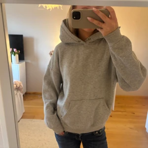 Grå hoodie från BikBok - Säljer en klassisk grå hoodie från BikBok i storlek S. Tröjan har huva, magficka och ribbade muddar vid ärmslut och nederkant. Perfekt för chill dagar eller när du vill ha något bekvämt och enkelt. Materialet är mjukt och känns skönt mot huden.